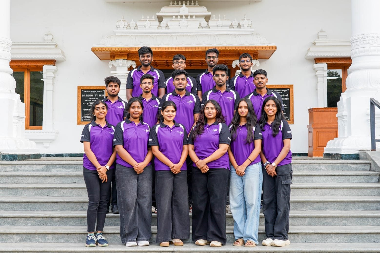 The AIRA Racing team in purple team polos, standing on the steps of a Kumaraguru College of Technology building